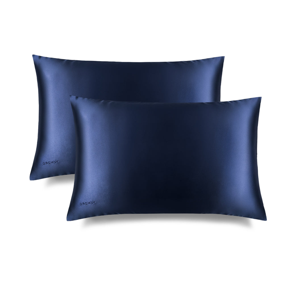 Two us.drowsysleepco Midnight Blue Silk Pillowcases, ideal for skincare and beauty, overlap on a white background. Both have a smooth, shiny finish and feature a small embroidered logo in one corner.