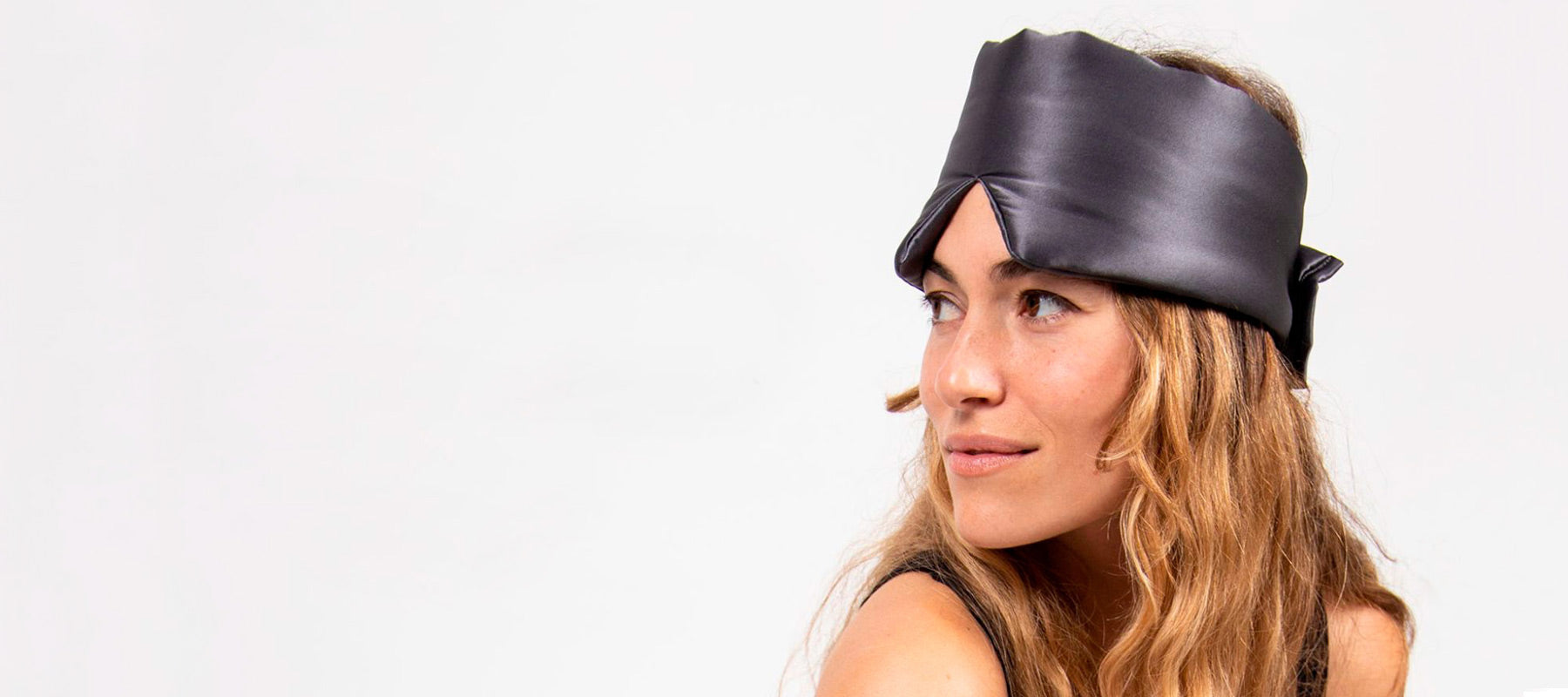 A woman with long wavy hair wears a black satin head wrap and looks off to the side against a plain white background.