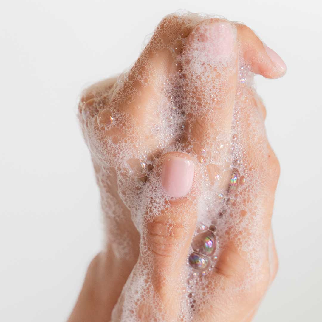 A hand with light pink nails is covered in foamy soap bubbles from us.drowsysleepco’s Beauty Sleep Body Cleanser, a night ritual wash infused with sleep-focused essential oils, shown against a plain white background.