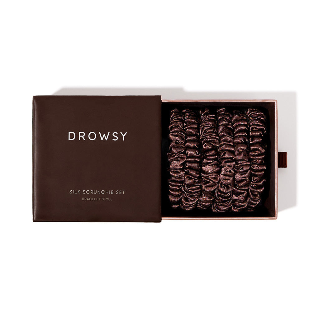 An open brown box labeled drowsysleepco Skinny Scrunchie Set - Cocoa Glow reveals several dark brown 22 momme silk scrunchies, neatly arranged for hair health and stylish comfort.