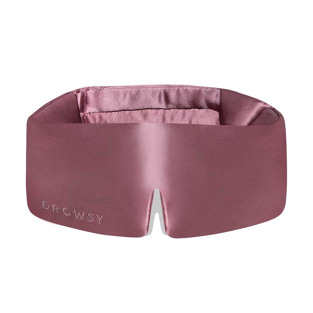The Damask Rose eye mask by us.drowsysleepco is wide, silky pink with Drowsy embossed on the front, a central notch, and a soft padded blackout interior for enhanced comfort and rest.