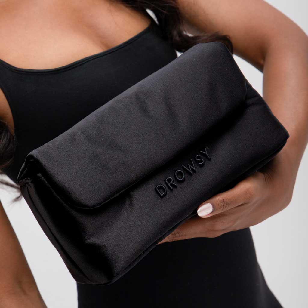 A person in a sleeveless black top holds the Drowsy Sleepover bundle - Black Jade pouch, featuring DROWSY embossed on the front. Their fingernails are painted pale pink.