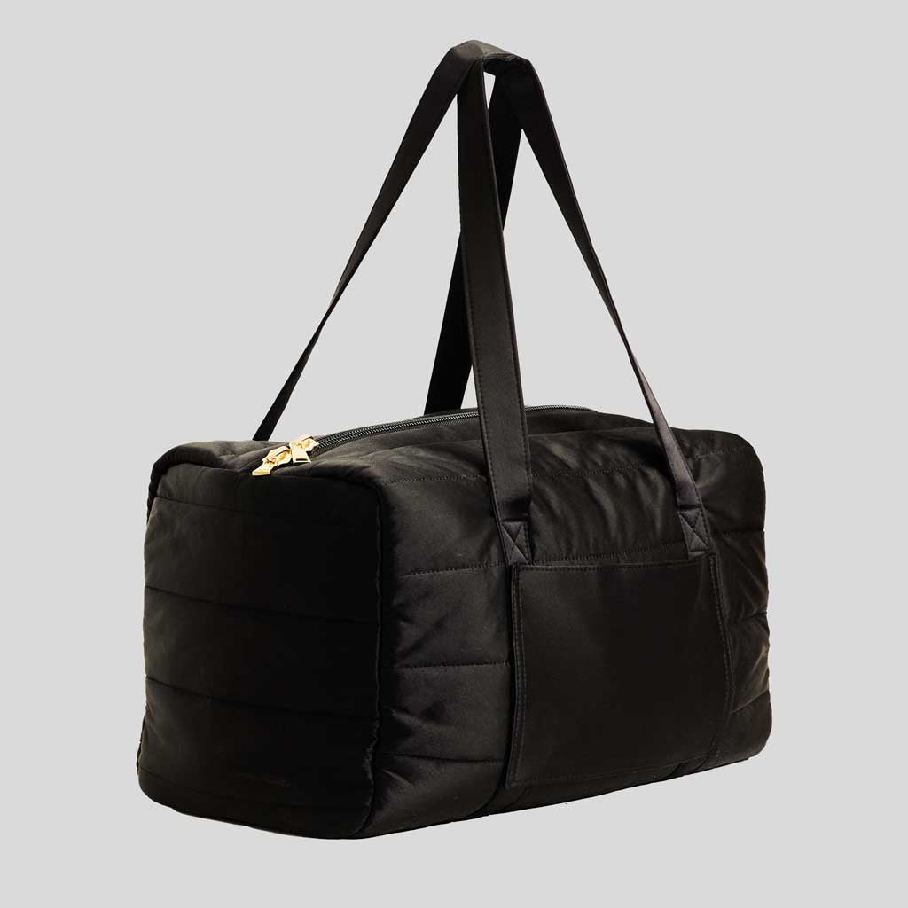 The Drowsy Silk Weekender - Black Jade is a spacious black quilted duffel with dual handles, zippered top, and side pocket—ideal for weekend trips—shown against a plain gray background.