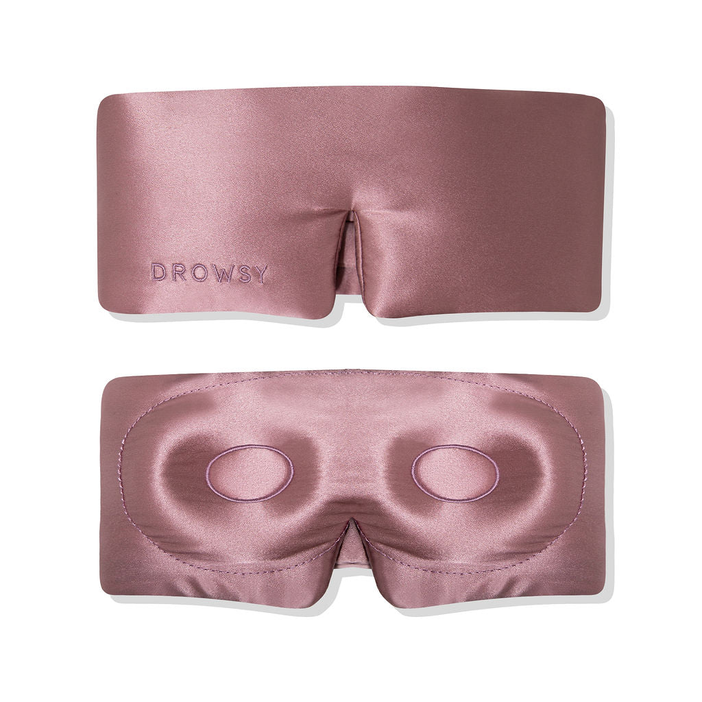 A silky, mauve-colored sleep mask shown from the front and back. The front is smooth with DROWSY embroidered on it, and the back has padded eye contours for comfort.