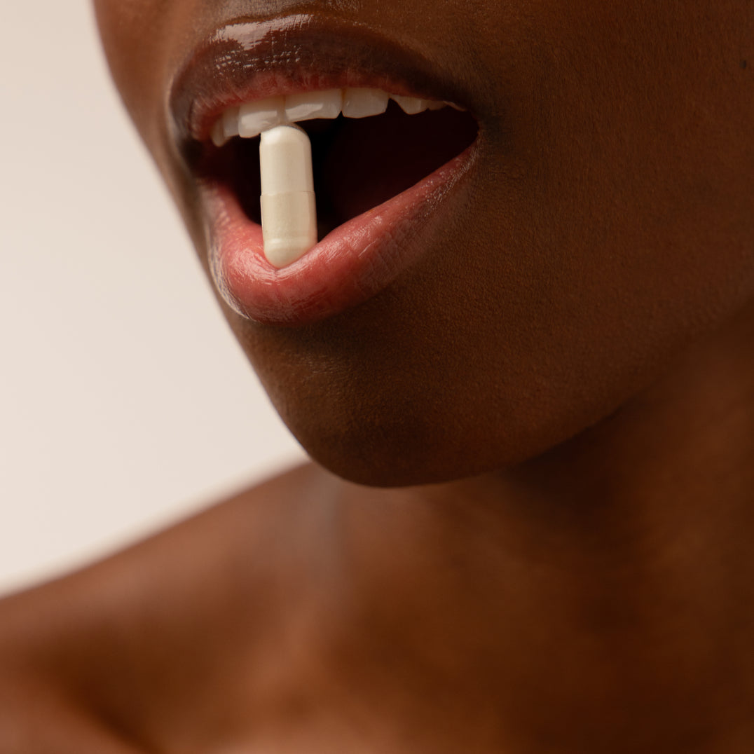 A close-up of a persons smooth-skinned mouth, slightly open and holding a white us.drowsysleepco Supplements - Beauty Sleep Clinic pill between their lips, with a soft, neutral out-of-focus background.