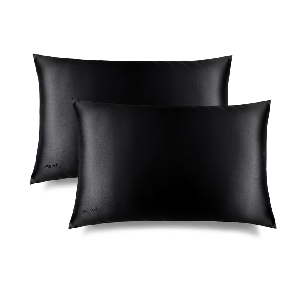 Two Black Jade Silk Pillowcases by us.drowsysleepco overlap on a white background, each featuring a subtle logo in the bottom left corner—luxurious essentials designed to protect your skin and hair while you sleep.