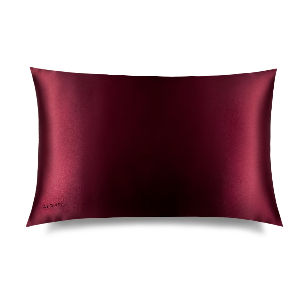The La Vie En Rouge Silk Pillowcase by us.drowsysleepco is a rectangular burgundy silk case with a smooth, shiny finish and a subtle embroidered logo in the bottom left corner, displayed against a white background. Perfect for protecting hair.
