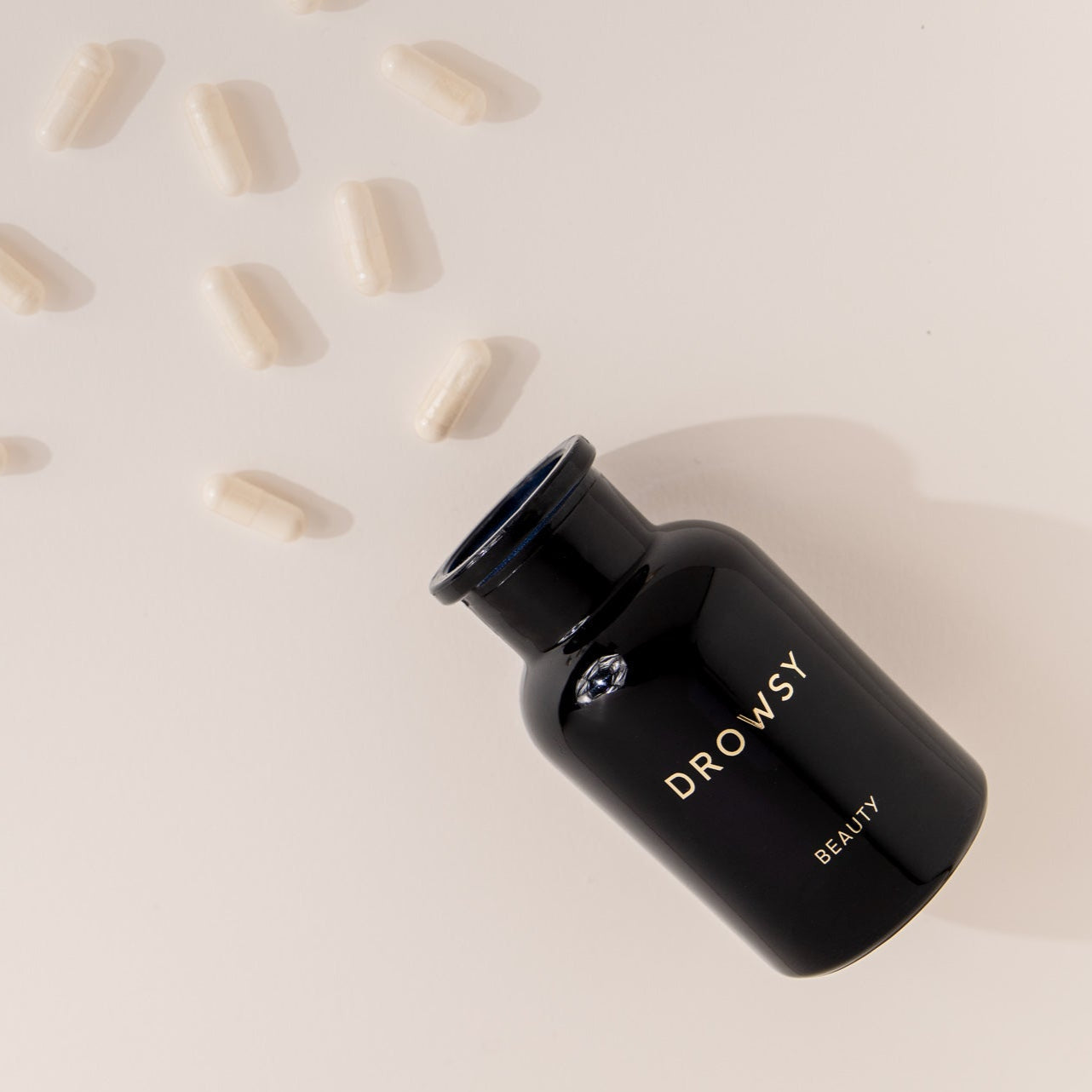 A black Apothecary Glass Storage Jar by drowsysleepco lies on its side with its cap off, while several white capsules are scattered nearby on a light surface.
