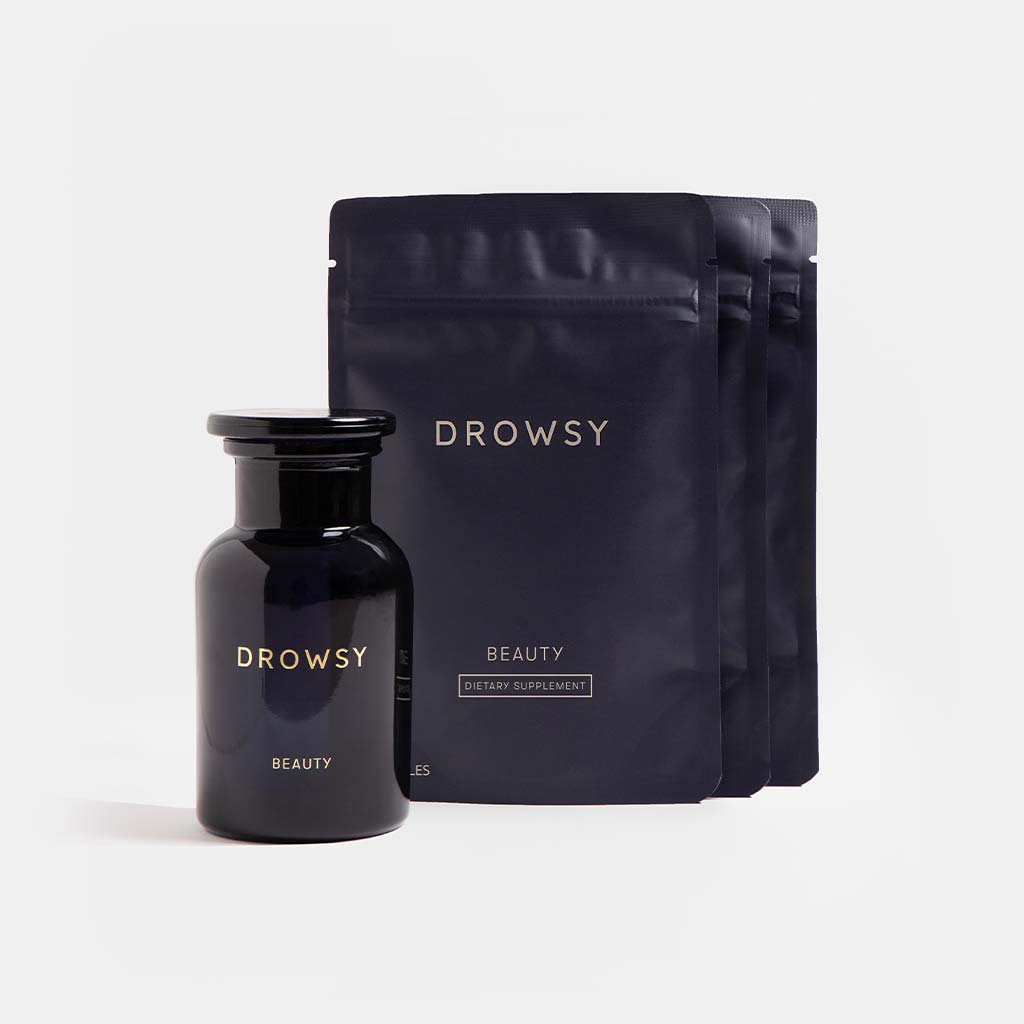 A dark glass bottle labeled Supplements - Beauty by us.drowsysleepco stands before three matching black sachets, both supporting collagen synthesis for a youthful complexion, set against a plain light background.