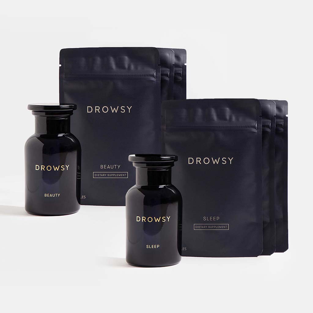 Two dark glass bottles and four matte black pouches from us.drowsysleepcos Supplements - Beauty Sleep Clinic are labeled “Beauty” for skin support or “Sleep” for restorative rest, all arranged on a plain, light background.