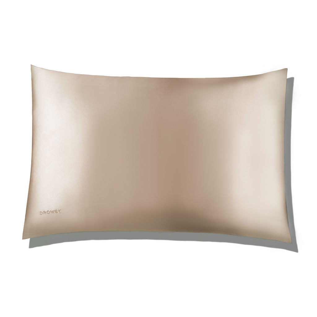 A smooth, light gold silk pillowcase with a subtle sheen, seen from above on a white background. The word DROWSY is embroidered in small letters in one corner.