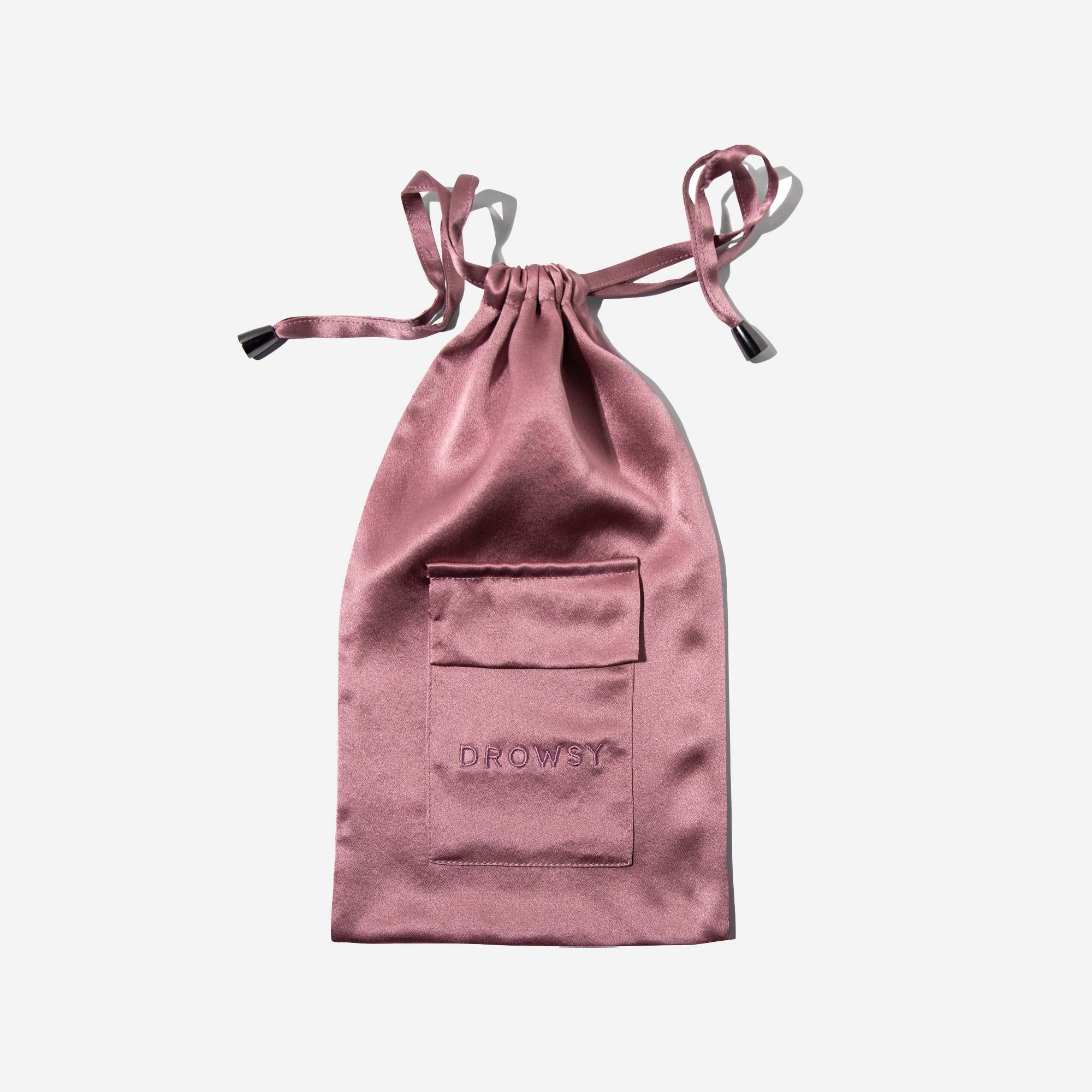 A pink satin drawstring pouch with a small pocket on the front and the word “DROWSY” embroidered on it, photographed against a white background.
