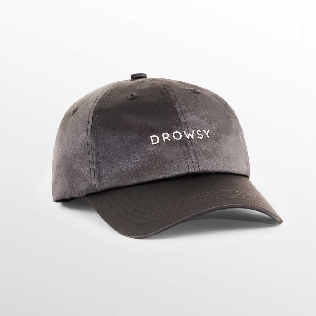The Drowsy Silk Cap - Moonlight Shadow by Drowsy features DROWSY embroidered in white on gray silk, offering stylish sun protection while keeping your hair flawless, shown against a soft gradient background.