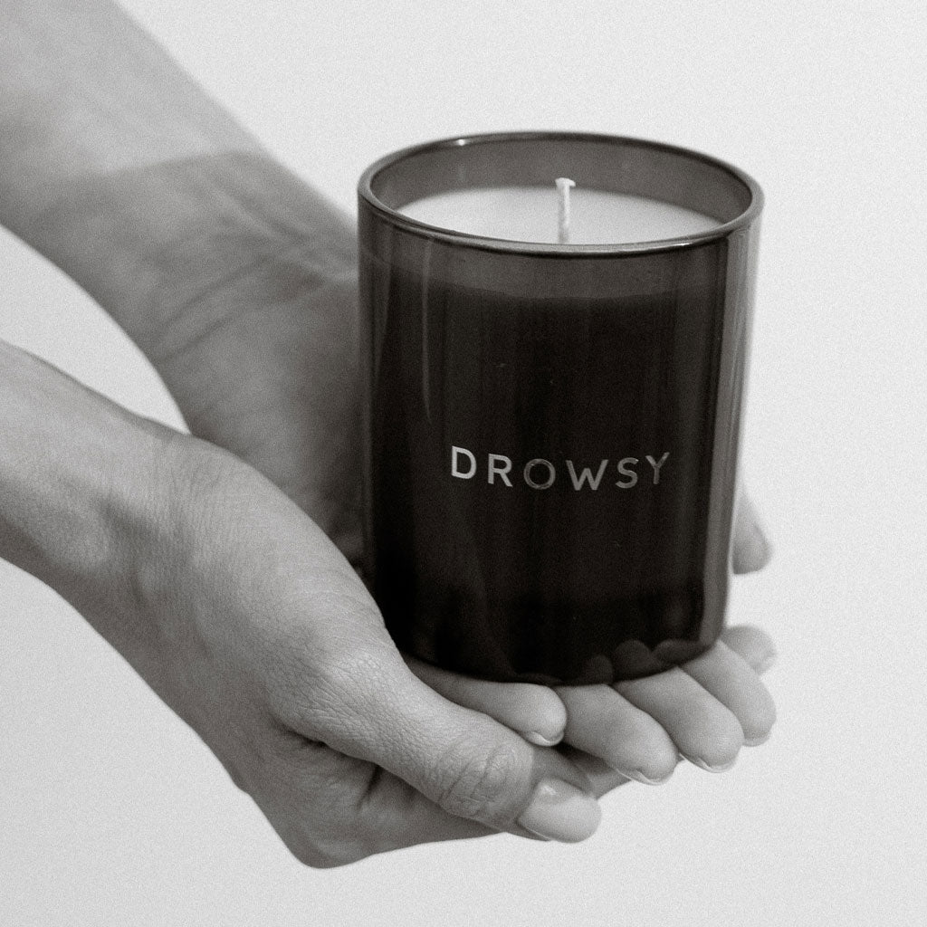 A person holds a dark glass jar of the drowsysleepco Sleep Ritual Candle 220g in both hands, captured in black and white—a serene scene evoking relaxation and pre-sleep rituals.