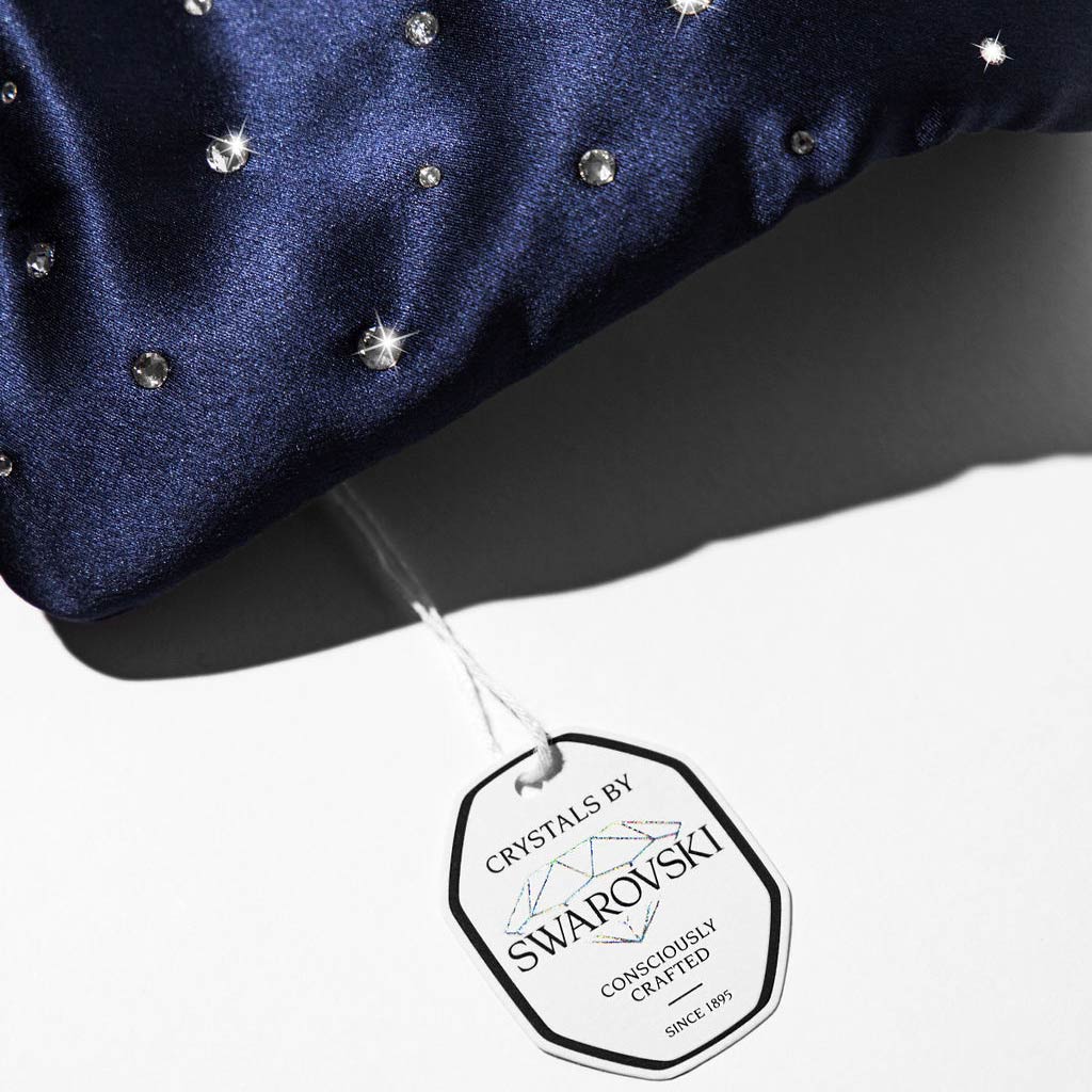 The Silk Sleep Eye Mask Crystals by Swarovski® from us.drowsysleepco is shown in navy satin silk with a 100% blackout design. It features Swarovski® crystals and a white tag reading Crystals by Swarovski, Consciously Crafted, Since 1895.
