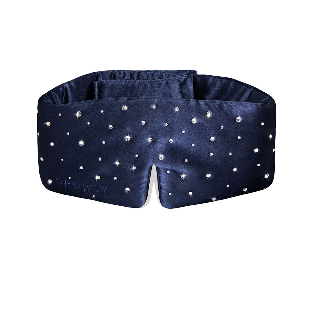The Silk Sleep Eye Mask Crystals by Swarovski® from us.drowsysleepco is a navy silk eye mask with sparkling Swarovski crystals, a wide padded design for 100% blackout, and Drowsy subtly embossed on the left side.
