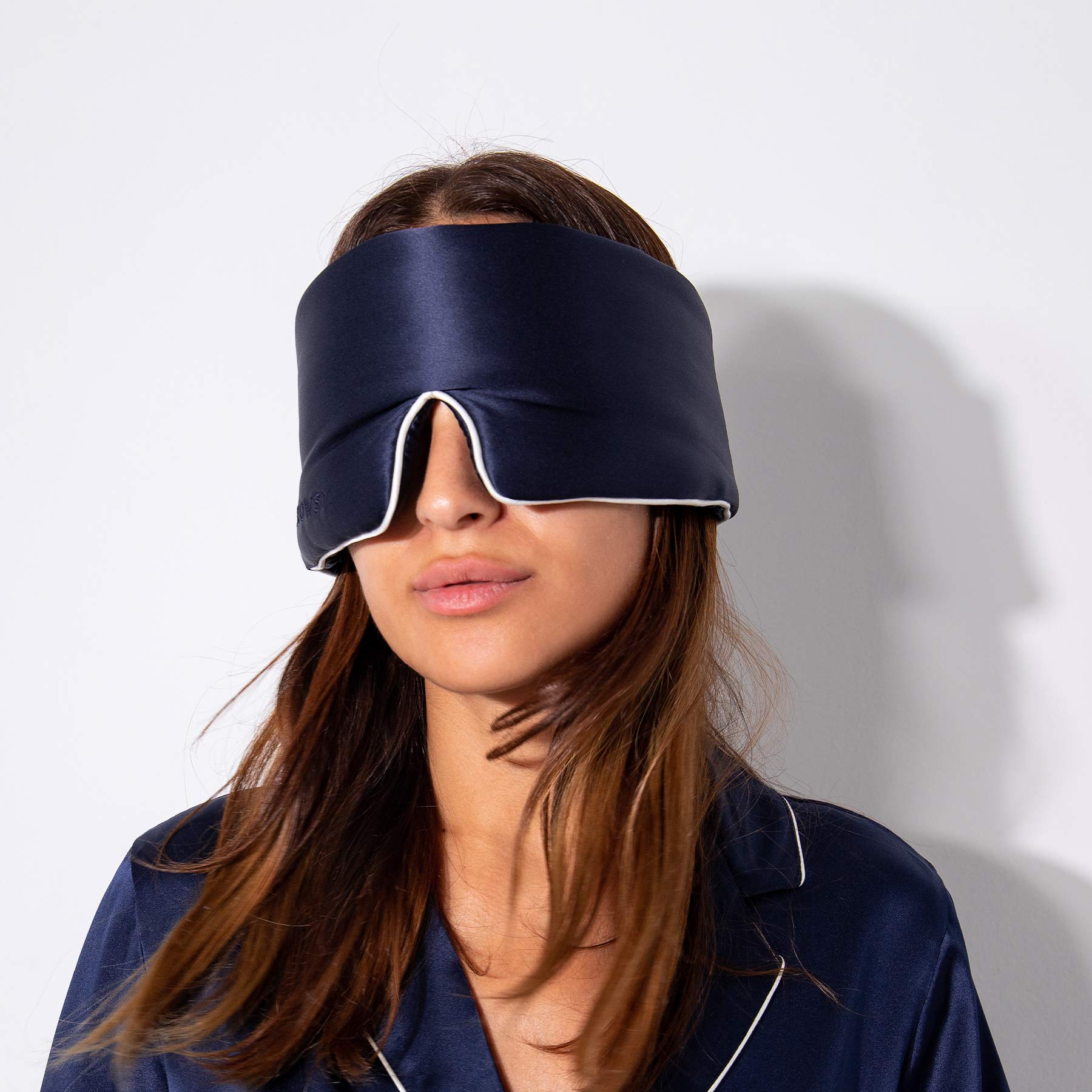 A woman wears us.drowsysleepcos Midnight Blue - Pipe Dreams Edition mulberry silk sleep mask with blackout design and white trim, covering her eyes and upper face against a plain white background.