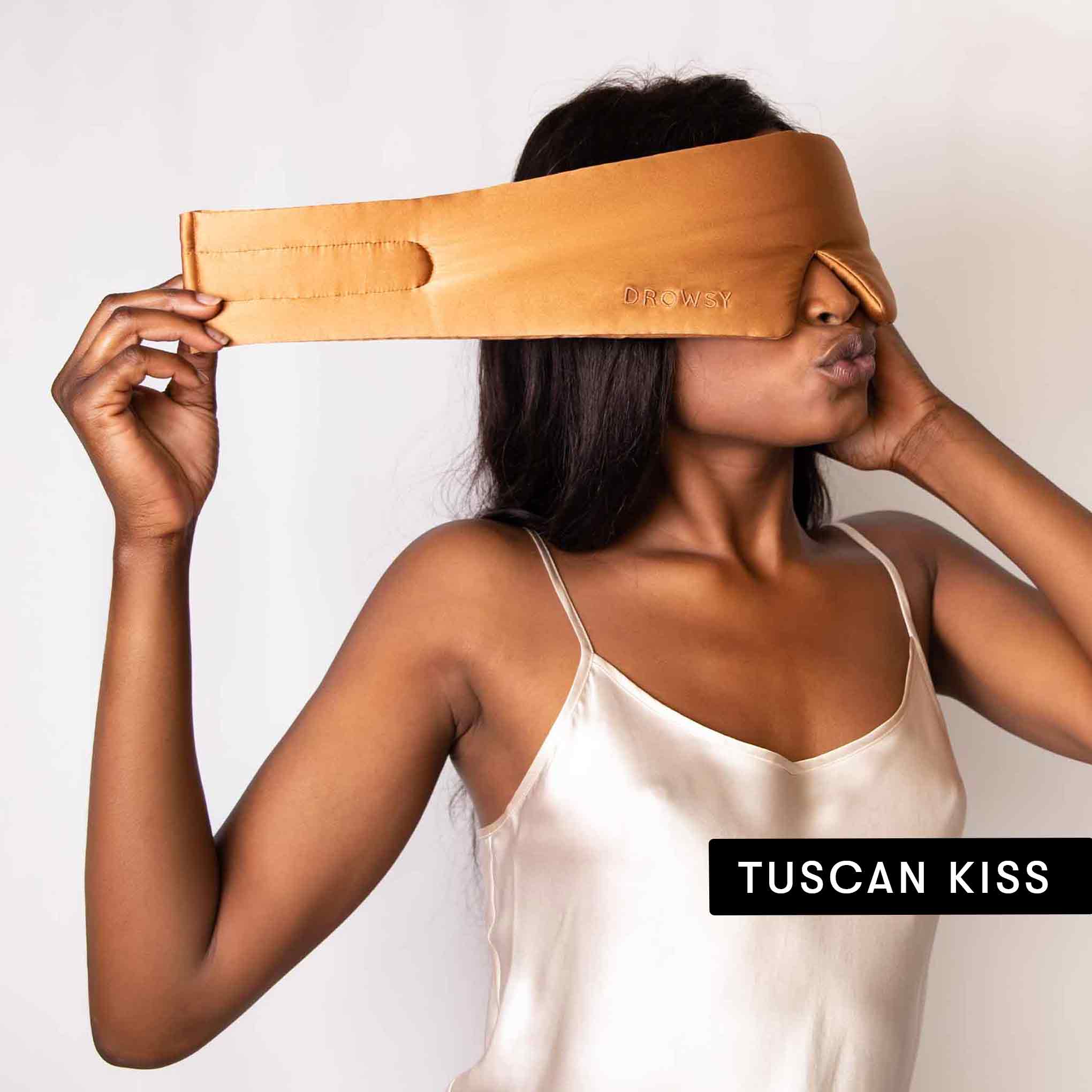 A woman in a satin camisole wears a tan Drowsy silk mask from the Lovers Pack, ideal for beauty sleep. TUSCAN KISS appears in the lower right corner.