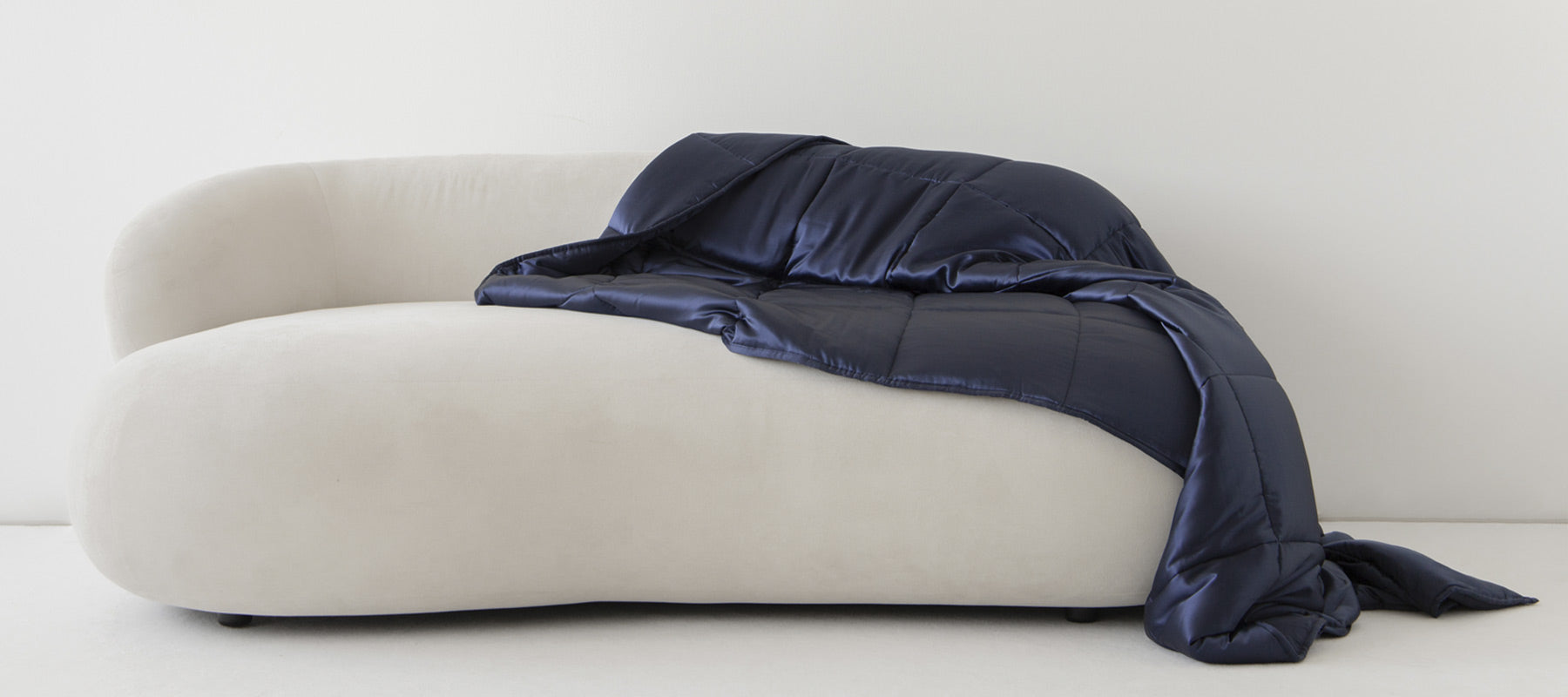 A plush, white, curved sofa sits against a plain wall with a dark navy blue blanket draped casually over one side.