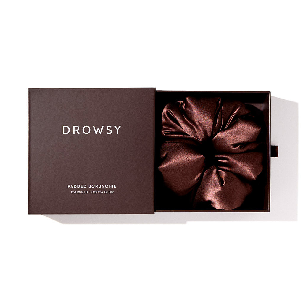 A dark brown box labeled us.drowsysleepco reveals the Cocoa Glow - Padded Scrunchie, a luxurious oversized silk hair accessory in rich cocoa, partially visible inside the open box on a white background.
