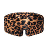 A woman outdoors wears the Hotel Paradiso Wild Thing Sleep Mask by us.drowsysleepco, featuring a leopard-print design. She stands beneath palm trees and blue sky, dressed in a dark lace top with long, dark hair.