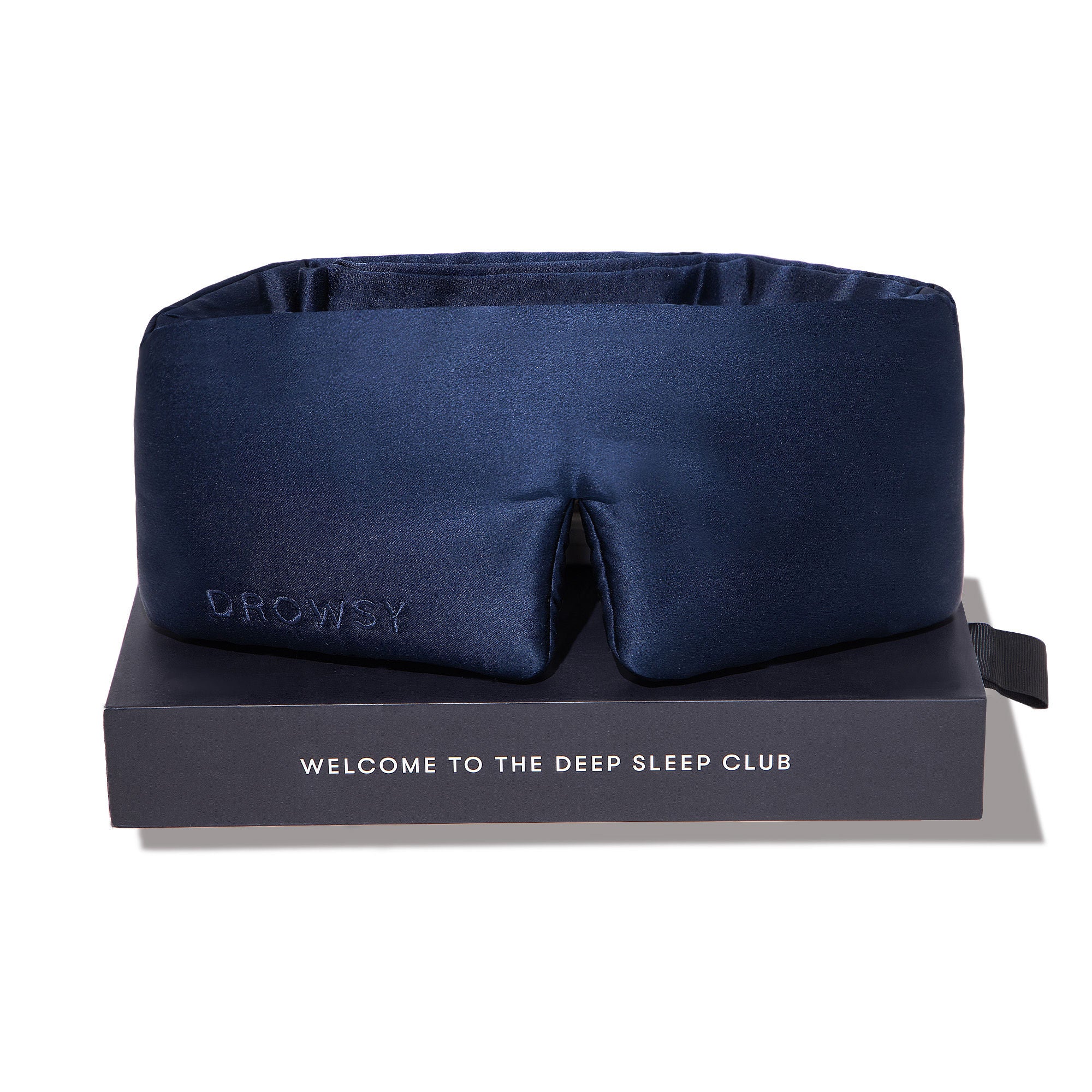 A dark blue sleep mask with the word DROWSY embossed on it, displayed on a black box that reads WELCOME TO THE DEEP SLEEP CLUB, against a white background.