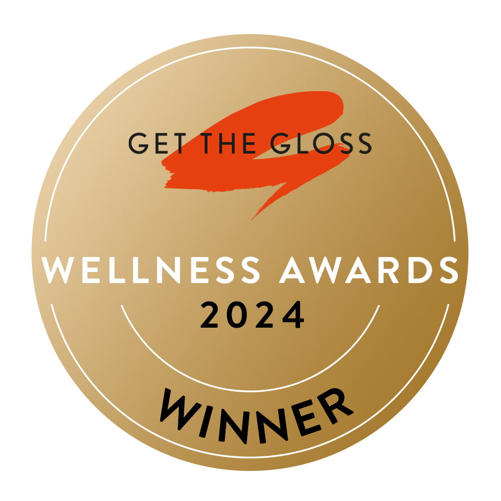 A gold circular badge with the text Get The Gloss Wellness Awards 2024 Winner in black and white, featuring a red brushstroke design and a gold border.