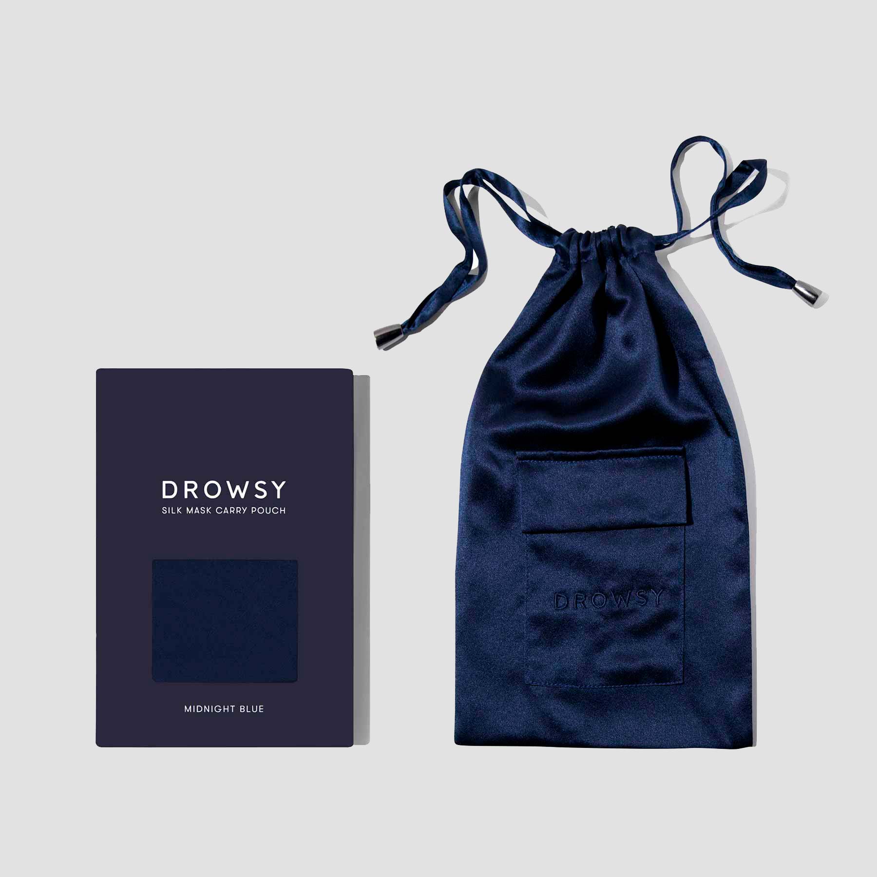 A navy blue silk pouch with a drawstring and pocket is placed next to a matching flat rectangular box labeled Drowsy Silk Mask Carry Pouch Midnight Blue on a light gray background.