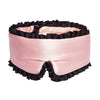 A woman with wavy hair lies on a pink satin pillow, wearing the drowsysleepco Sleep and the City Pink & Black mulberry silk blackout sleep mask with 