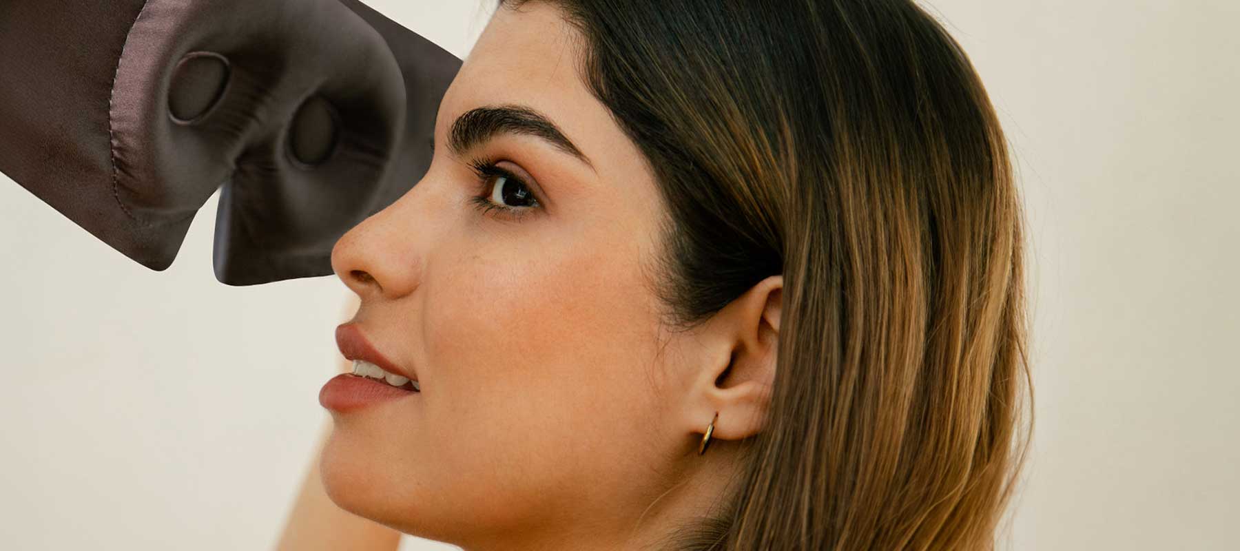 A close-up of a woman with long brown hair and gold hoop earrings, looking to the side and smiling slightly, as a boxing glove approaches her face from the left.